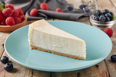 Mavi plaka üzerinde klasik düz New York Cheesecake kapatın. Lezzetli ev yapımı peynir pasta üzerinde ahşap rustik antika arka plan bulanık ahududu ve yaban mersini ile üçgen dilimi