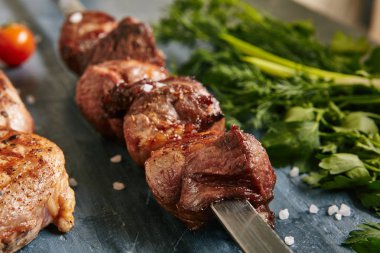 Derin kızarmış altın kuzu kebabı veya Barbekü şaşlık şiş baharatlar ile üzerinde kapatın. Makro fotoğraf saptırılmış ızgara küpleri koyun eti taze yeşillikleri ile siyah arka plan üzerinde seçici odak ile