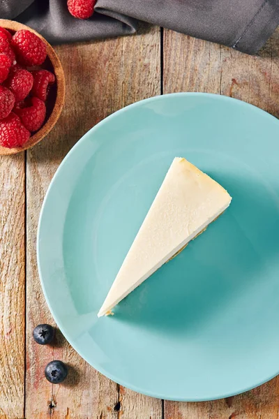 ブルー プレート上面にクラシック プレーン ニューヨーク チーズケーキ おいしい自家製チーズ ケーキにラズベリーとブルーベリーの木製の素朴なヴィンテージ背景ぼけの三角形のスライス — ストック写真