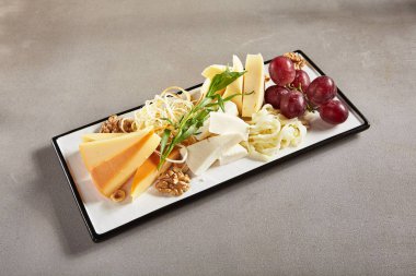 Wine Plate with Cheese Mix, Nuts and Grapes on White Rectangular Flat Plate. Cheeseboard with Pieces of Various Cheese such as Cheddar, Manchego, Gauda and Smoked Cheese clipart