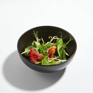 Makro fotoğraf gevrek sebzeler yeşil beyaz arka plan üzerinde izole siyah yuvarlak kase içinde karıştırın. Dilimlenmiş domates, Soya filizi, taze ıspanak yaprakları ve Genç bezelye çekimleri ile Restoran başlangıç menüsü