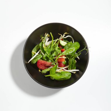 Makro fotoğraf gevrek sebzeler yeşil beyaz arka plan üzerinde izole siyah yuvarlak kase içinde karıştırın. Dilimlenmiş domates, Soya filizi, taze ıspanak yaprakları ve Genç bezelye çekimleri ile Restoran başlangıç menüsü