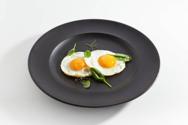Kızarmış yumurta taze ıspanak yaprakları ve düz siyah plaka üzerinde genç bezelye çekimleri ile dekore edilmiş zarif restoran tabak. Sağlıklı besleyici kahvaltı beyaz arka plan üzerinde izole makro fotoğraf