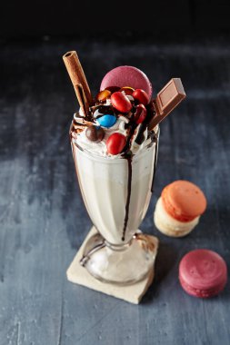 Deli Milkshake veya çikolata davranır, Macaroons ve renkli tatlılar Mix uzun bardak restoranda servis ile Freakshake. Tatlı tatlı içki süt canavar ya da ucube Shake denilen siyah arka plan üzerinde