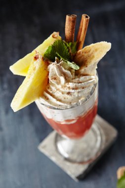 Sıcak meyve kokteyli ile ananas taze, muz, tarçın, nane yaprakları ve krem şanti siyah arka plan üzerine kapatın. Makro fotoğraf sıcak tatlı kış kokteyl uzun bardak restoranda servis