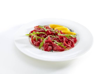Kurutulmuş İtalyan sığır Bresaola, limon, taze fesleğen, roka ve balsamik krem beyaz arka plan üzerinde izole. Air-dried ve tuzlu Dana, at, geyik eti veya domuz eti ile Yeşiller düz Restoran plaka üzerinde