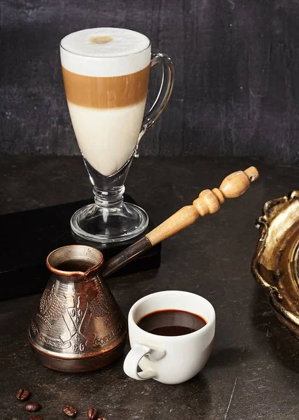 土耳其咖啡壶和香料浓缩咖啡在白杯与拿铁在高玻璃在黑暗复古背景 Macchiato Mocha 或卡布奇诺与奶油在天然黑石关闭 — 图库照片