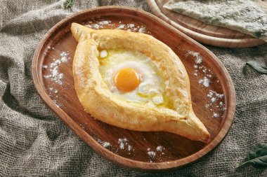 Çiğ yumurta ve erimiş tereyağı ile doldurulmuş sulguni peynirli ev yapımı Ajarian Khachapuri. Taze Gürcistan Geleneksel Peynir Doldurulmuş Tekne Biçiminde Ekmek
