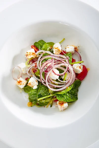 Green Salad with Goat Cheese, Spinach, Tomato and Red Onion Rings Isolated on White Background. Restaurant Starter Menu with fresh Spinacia and Chard Leaves, Tomatoes, Greens, Spices Top View