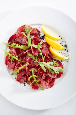 Kurutulmuş İtalyan sığır Bresaola, limon, taze fesleğen, roka ve balsamik krem üstten görünüm. Air-dried ve tuzlu Dana, at, geyik eti veya domuz eti ile Yeşiller düz Restoran plaka üzerinde