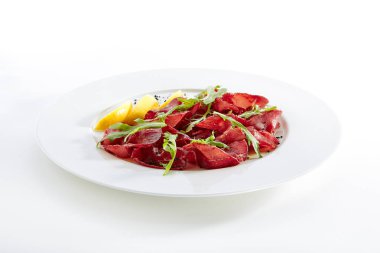 Kurutulmuş İtalyan sığır Bresaola, limon, taze fesleğen, roka ve balsamik krem beyaz arka plan üzerinde izole. Air-dried ve tuzlu Dana, at, geyik eti veya domuz eti ile Yeşiller düz Restoran plaka üzerinde