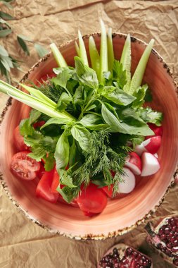 Vegan tabak taze dilimlenmiş salatalık, yeşil soğan, turp, domates ve tatlı biber güzel seramik tabak üstten görünüm koydu. Sulu organik sebze fesleğen, dereotu, maydanoz ile