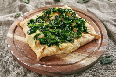Homemade Square Khachapuri Made From a Delicious Tender Dough with Spinach, Melted Cheese and Butter Close Up. Traditional Hachapuri Topped with Spinacia Leaves on Wooden Rustic Background clipart