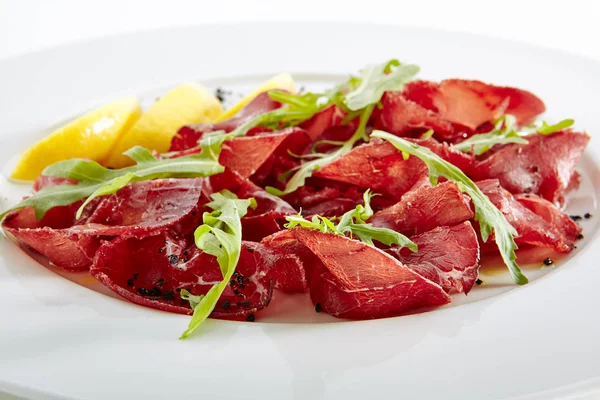 Сушеная итальянская говядина Bresaola с лимоном и зелеными изолированы — стоковое фото