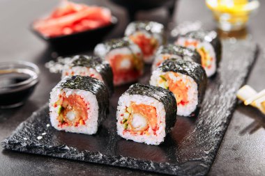 Pirinç, somon, kızarmış karides, salatalık, uçan balık havyar, baharatlı sos ve nori ile uramaki suşi rulo Makro atış. Japon restoran closeup sıcak baharatlı suşi rulo holding