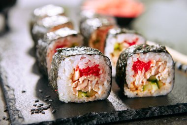 Chopsticks closeup ile Japon restoranında suşi rulo Makro atış. Pirinç, kızarmış somon, uçan balık havyar, salatalık ve baharatlı sos ile Suşi rulo