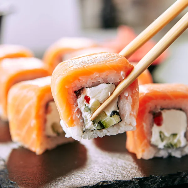 Chopstick Holding Sushi Rolls Set Salmon Cream Cheese Cuccumber Black — Stock Photo, Image
