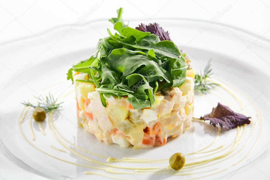Classic Olivier salad or Russian salad with chicken fillet, quail eggs, pickles, greens and peas on white plate isolated. Traditional Christmas salat or Stolichny salad on a white plate in restaurant closeup