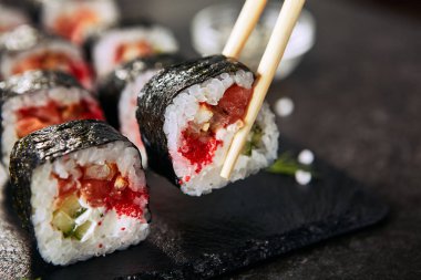 Krem peynir, somon, geyik balığı, pirinç, salatalık, uçan balık havyar ve nori ile dragon rulo tutan Chopstick. Doğal koyu taş arka plan üzerinde çiğ kırmızı balık ve tobiko ile Dragon unagi maki rulo yakın