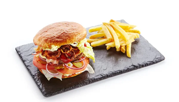 新鲜牛肉汉堡配培根 炸洋葱 番茄酱 腌黄瓜 绿生菜 芝士和法式薯条装饰 在白色的天然黑石板上的汉堡包或 Beefburger — 图库照片