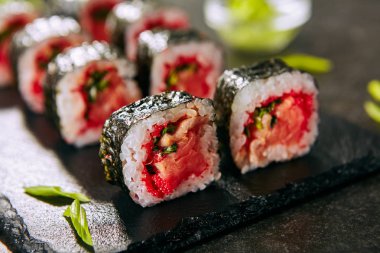 Yeşil soğan, uçan balık kırmızı havyar, baharatlı sos ve bulanık arka plan üzerinde nori ile füme somon suşi rulo Makro atış. Siyah kayrak plaka arka plan closeup taze gurme Japon gıda