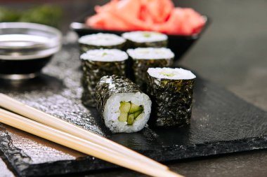Seçici odak ile doğal siyah kayrak plaka arka plan üzerinde soya sosu ile hosomaki suşi Makro çekim. Salatalık, pirinç, susam ve nori closeup ile Kappa maki suşi rulo