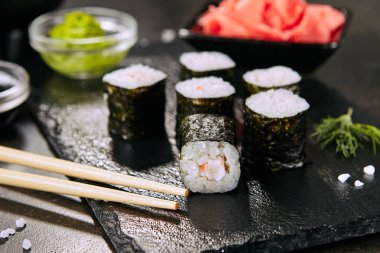 Seçici odak ile doğal siyah kayrak plaka arka plan karides hosomaki suşi Makro çekim. Pirinç, kral karides ve nori closeup ile ince küçük maki suşi rulo
