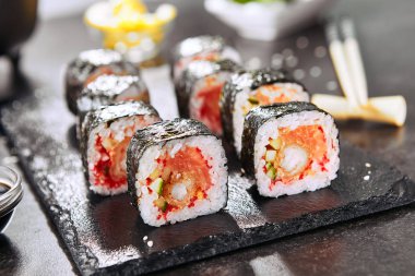Pirinç, somon, kızarmış karides, salatalık, uçan balık havyar, baharatlı sos ve nori ile uramaki suşi rulo Makro atış. Japon restoran closeup sıcak baharatlı suşi rulo holding