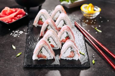Pirinç, krem peynir, füme somon, domuz yağı, salatalık, yeşil soğan, nori ile pastırma uramaki suşi rulo Makro atış. Japon restoran closeup yemek çubukları ile Sushi rulo
