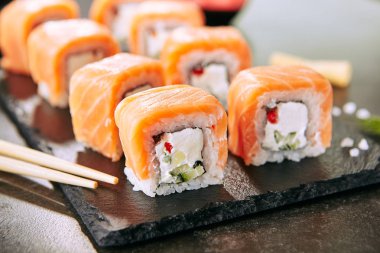 Güzel Philadelphia Sushi Rolls Set Somon ve Krem Peynir ve Cuccumber Black Slate Plate Close Up üzerinde. Uramaki, Nori Maki veya Futomaki Suşi Alabalık Fileto, Soya Sosu ve Wasabi ile