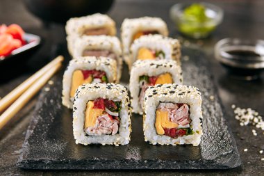 Gökkuşağı uramaki suşi rulo pirinç, pastırma, işlenmiş peynir, domates, yeşil soğan, susam ve nori siyah kayrak plaka arka plan closeup üzerinde. Japon restoranında füzyon maki suşi Makro çekim