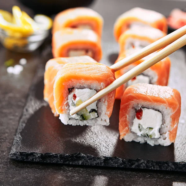 Chopstick Holding Sushi Rolls Salmon Cream Cheese Cuccumber Black Slate — Stock Photo, Image