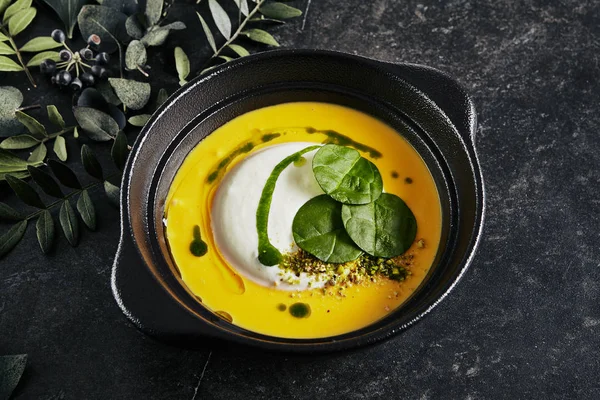 Exquisite Serving Pumpkin Cream Soup with Ricotta Cheese Mousse Close Up. Beautiful Creative Molecular Italian Dish with Stylish Decorations of Dark Plants on Natural Black Stone