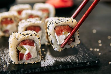 Chopsticks pirinç, krem peynir, domates, salatalık, susam ve nori yakın tokyo somon uramaki suşi tutan. Füme balık ve taze sebze ile Japon gıda uramaki rulo Makro atış