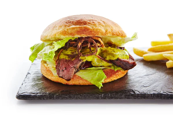 经典的烤牛肉汉堡配芥末 炸洋葱 绿色萨尔萨酱和法式薯条装饰 Beefburger 与中稀有牛排天然黑石板上隔绝白色 — 图库照片