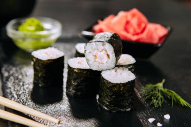 Seçici odak ile doğal siyah kayrak plaka arka plan karides hosomaki suşi Makro çekim. Pirinç, kral karides ve nori closeup ile ince küçük maki suşi rulo