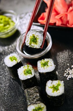 Seçici odak ile doğal siyah kayrak plaka arka plan üzerine yosun hosomaki suşi daldırma Makro çekim. Pirinç, wakame, yosun salatası veya chuka ve nori closeup ile ince küçük maki suşi rulo