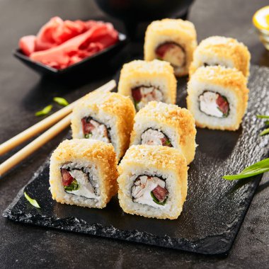 Füme tavuk, krem peynir, yeşil soğan, domates, pirinç ve nori ile tempura uramaki suşi rulo Makro atış. Siyah taş kayrak arka plan closeup sıcak gevrek maki rulo tutan chopsticks