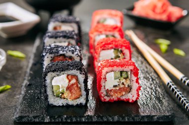 Pirinç, krem peynir, somon, deniz yıldızı, salatalık, uçan balık havyar ile maki suşi rulo Makro fotoğraf. Nori maki rulo ham alabalık, kırmızı ve siyah tobiko doğal koyu taş arka plan yakın