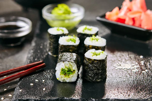 Macro shot of seaweed hosomaki sushi on natural black slate plate background with selective focus. Thin small maki sushi rolls with rice, wakame, kelp salad or chuka and nori closeup