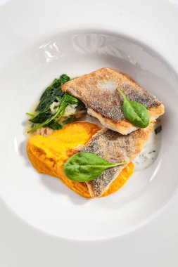 Balkabağı püresi ve ıspanak soslu morina filetosu. Deniz ürünleri restoranının menüsü. Lezzetli sağlıklı yiyecekler. Beyaz arka planda izole edilmiş enfes bir yemek. Gurme yemeği, lezzetli öğle yemeği. Yakın plan.