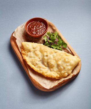 Domates soslu ve maydanozlu Cheburek. Geleneksel Rus hilal şeklinde etli turta. Ukrayna birası. Kızarmış etli börek. Lezzetli dolgulu hamur işi. Ahşap tepside servis edilen kafe tabağı.