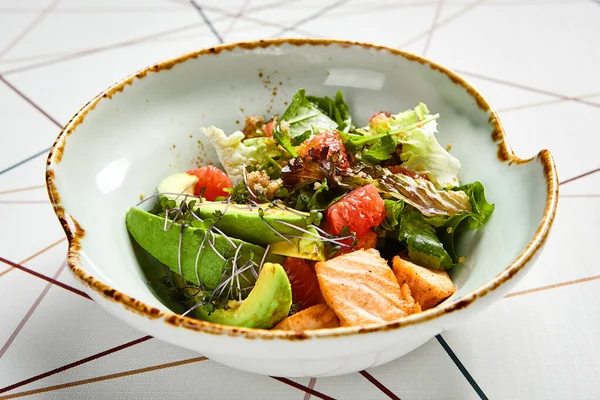 Luxury restaurant side dish top view. Salad with salmon and avocado. Fish and vegetable mix. Entree addition. Delicious meal course in deep craft plate. Fancy gourmet food overhead shot