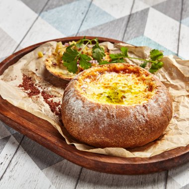 Yuvarlak ekmekli peynirli çorba. Maydanozla süslenmiş parşömen üzerinde fırınlanmış tabak. Güzel bir yemek, yakın plan servis ediliyor. Peynir dolgulu ekmek manzaralı. Ahşap tepside Khachapuri bölümü