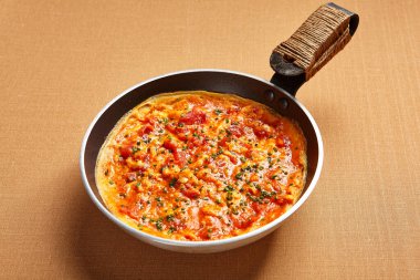 Domatesli ve baharatlı omlet. Demir tavada servis edilen soslu çırpılmış yumurtalar. Aşçılık sanatı. Taze otlarla süslenmiş taze yemek. Lezzetli sağlıklı kahvaltı. Lezzetli yemek.