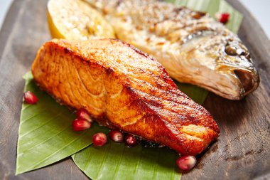 Tahta kırsal tabakta servis edilen balıklar. Izgara deniz kabuğu ve nar tohumları serpiştirilmiş bitki yaprakları üzerine somon balığı. Süslü restoran yemeği. Süslü deniz ürünleri tabağı. Yemek pişirme sanatı