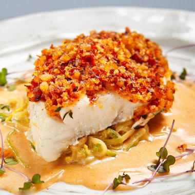 Soslu kızarmış morina filetosu. Restoran yemeği bölümü. Beyaz tabak üzerinde servis edilen hamurlu garnitürlü balık. Ekmek kırıntıları serpiştirilmiş deniz ürünleri. Lüks gurme yemek servisi