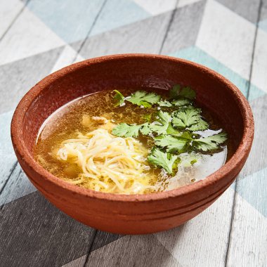 Kahverengi çanak çömlek içinde klasik tavuk suyu çorbası. Erişteli lezzetli çorba ve ahşap masadaki seramik tabakta kümes hayvanları. Tavuk çorbası sundum. Restoran yemeği kursu.