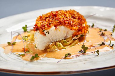 Soslu kızarmış morina filetosu. Restoran yemeği bölümü. Beyaz tabak üzerinde servis edilen hamurlu garnitürlü balık. Ekmek kırıntıları serpiştirilmiş deniz ürünleri. Lüks gurme yemek servisi