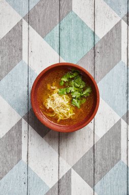 Kahverengi çanak çömlek içinde klasik tavuk suyu çorbası. Erişteli lezzetli çorba ve ahşap masadaki seramik tabakta kümes hayvanları. Tavuk çorbası sundum. Restoran yemeği kursu.